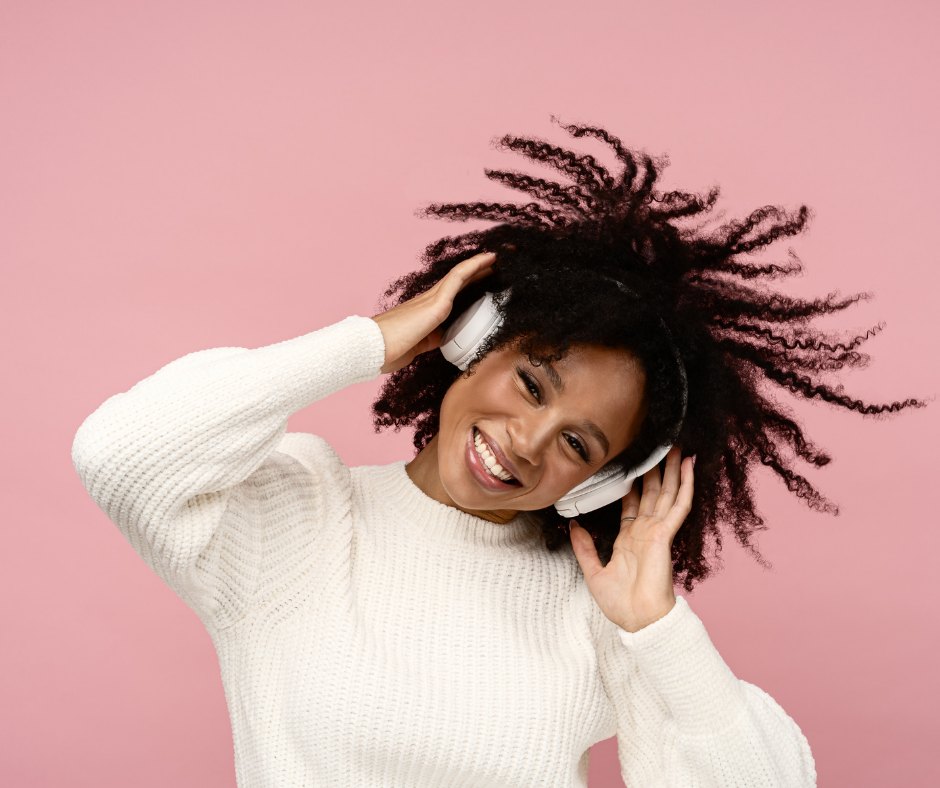 A listener smiling in white headphones against a pink backdrop
