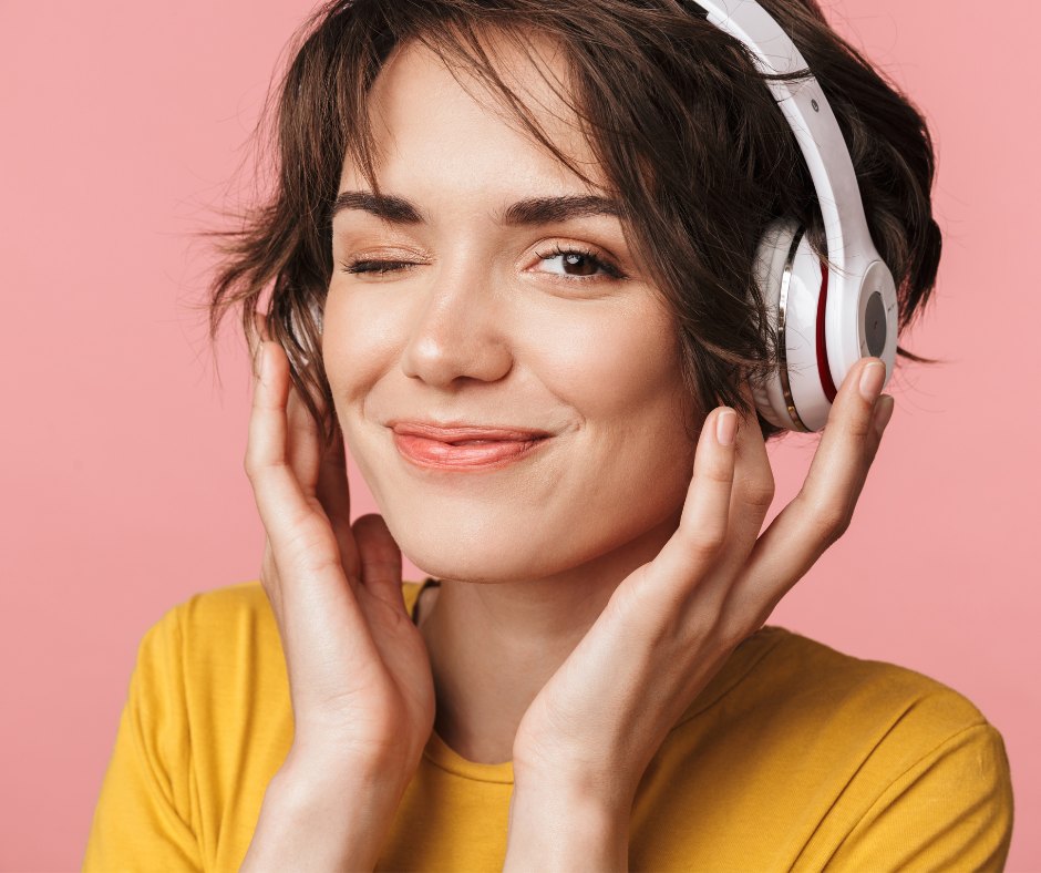 A listener smiling in white over-ear headphones against a warm pink backdrop